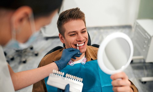 a dentist color-matching veneers to a patient’s teeth