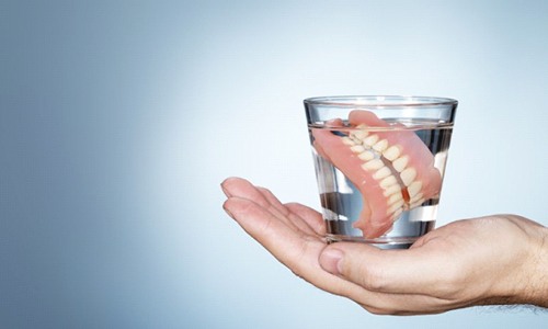 hand holding full denture in glass of water