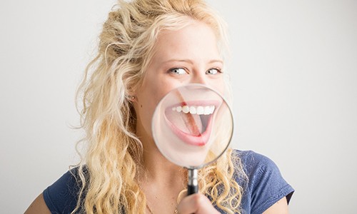 A young woman holding a magnifying glass up to her smile to show the results of gum recontouring