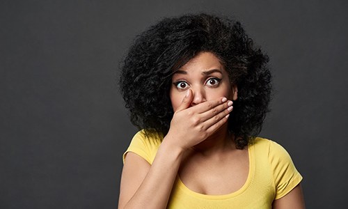 A young woman wearing a yellow shirt and covering her mouth