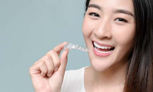 A young woman smiling and holding a top Invisalign aligner for her teeth