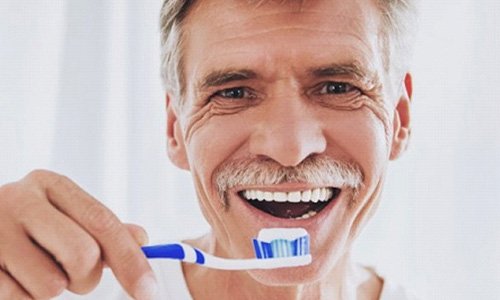 older man in white shirt brushing his teeth to prevent dental emergencies in Braintree