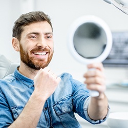 Man in blue shirt smiling while looking in dentist's mirror