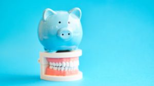 Blue piggy bank atop model jaw with dental implants in Braintree