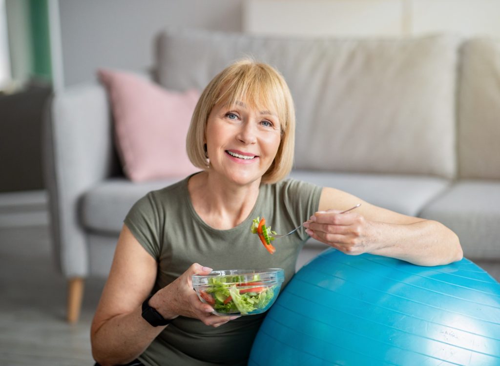Closeup of woman with dentures eating salad in living room