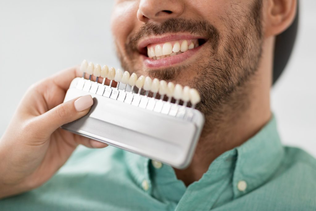 Man smiling while dentist matches shade of veneers