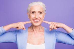 an older patient smiling and pointing toward her teeth